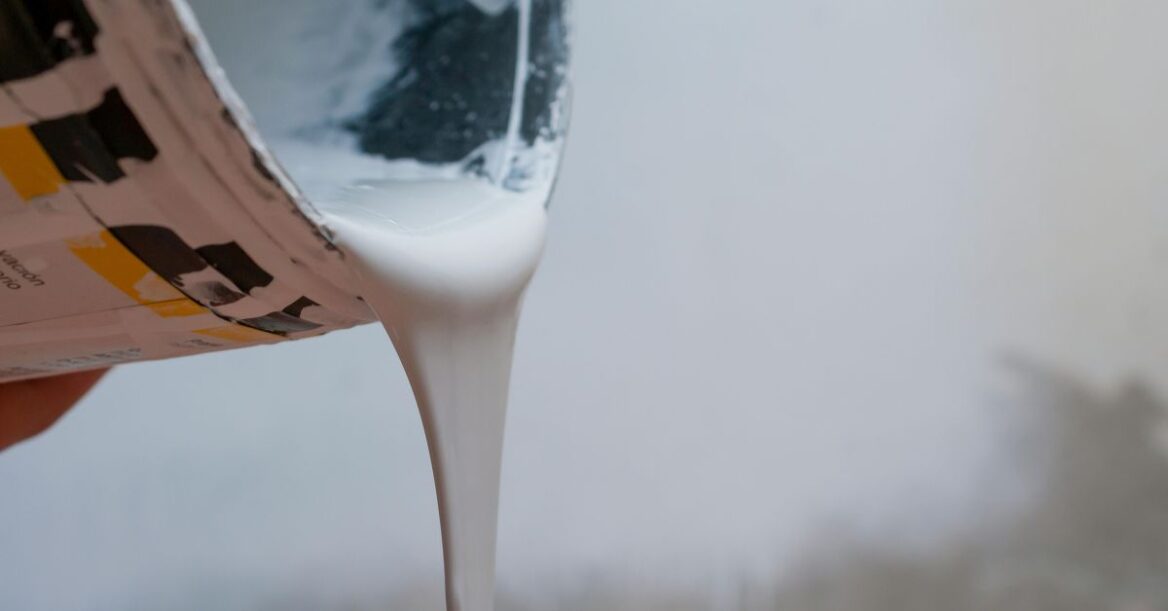 Close-up of white paint being poured from a can against a neutral background.