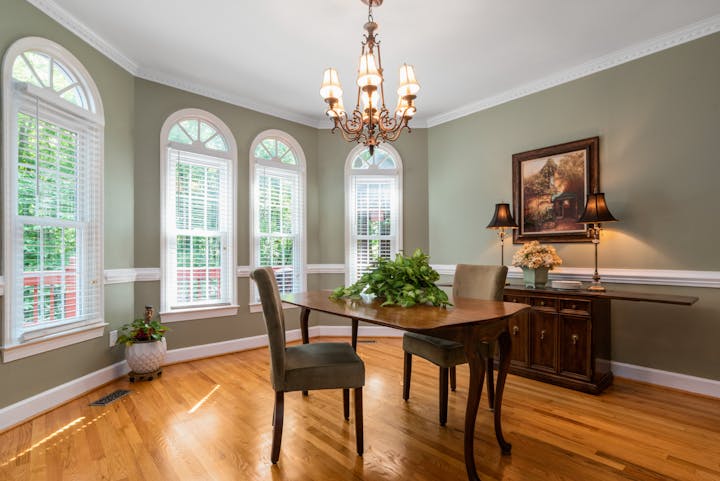 Elegant dining room with green walls, arched windows, wooden floor, chandelier, and a classic wooden dining table with two chairs.