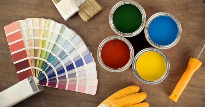 Various paint cans, tools and a color chart in brown wood background.