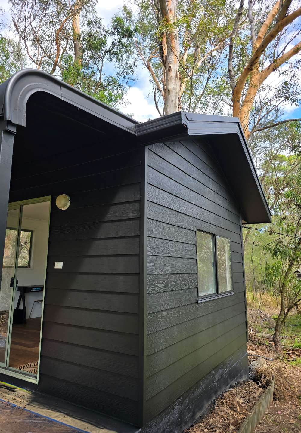 A close-up side view of a black-painted cabin with fresh cladding, showing a small window and clean roofline.