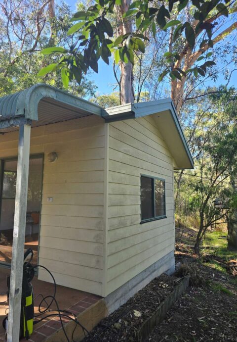 The side of a beige cabin with aged cladding and dirt marks, showing signs of wear before repainting.