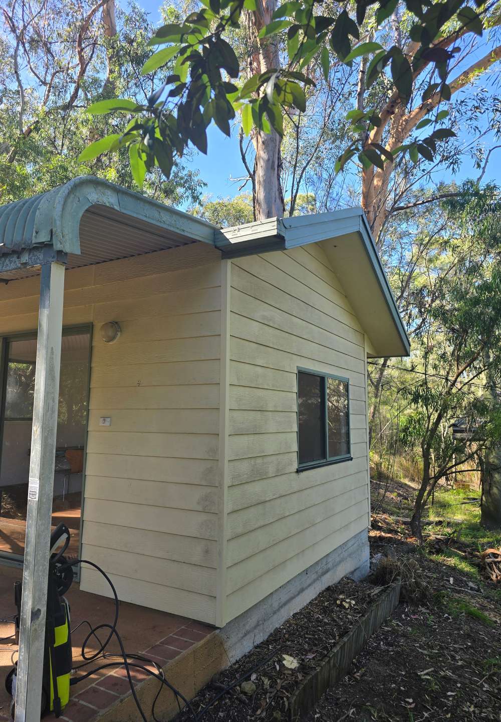 The side of a beige cabin with aged cladding and dirt marks, showing signs of wear before repainting.