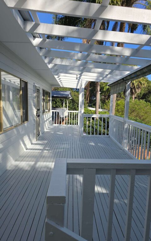 A large outdoor deck painted white with a pergola overhead, attached to a light-colored house.