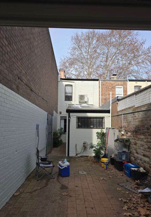 The back view of a terrace house with freshly painted white brick walls and clean paving in a narrow courtyard.